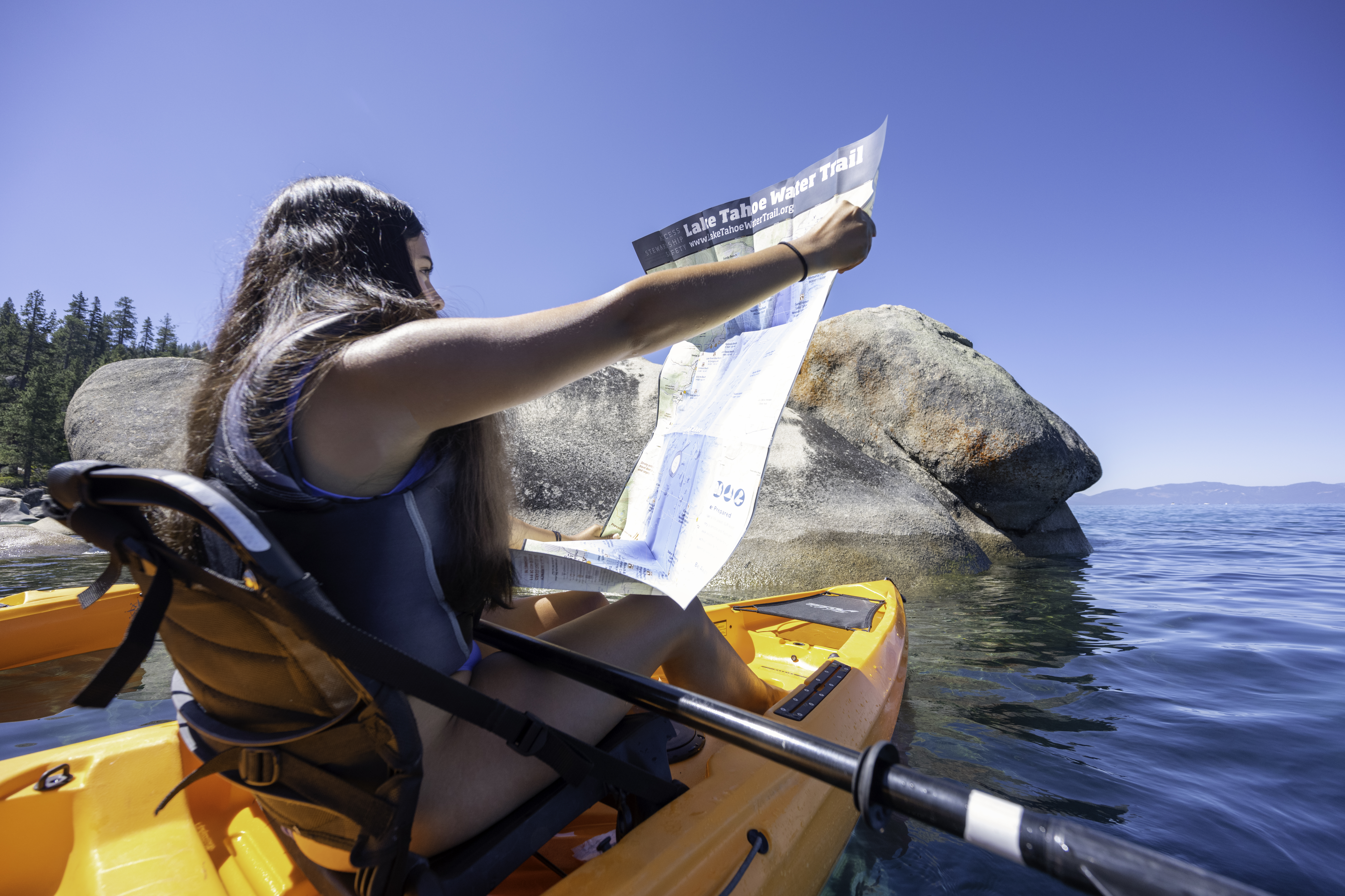 kayaker looking at Lake Tahoe Water Trail map next to a granite rock